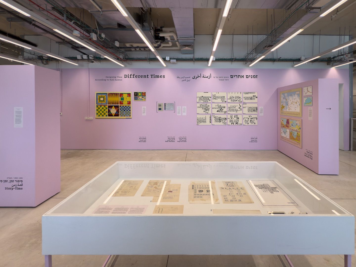View across the gallery: a glass display case in front of the pink title wall with framed calendars