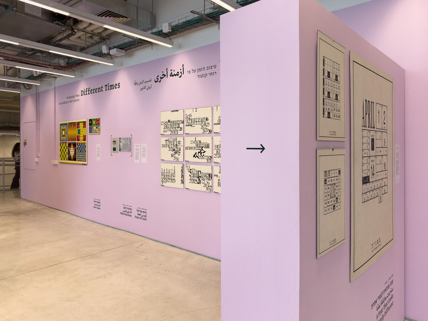 A pink wall with a grid of calendar pages, and a freestanding wall with large calendar prints and an arrow